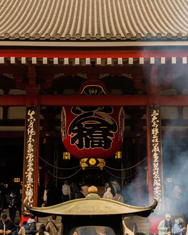 incense smoke drifts past the lantern while the crowd files through