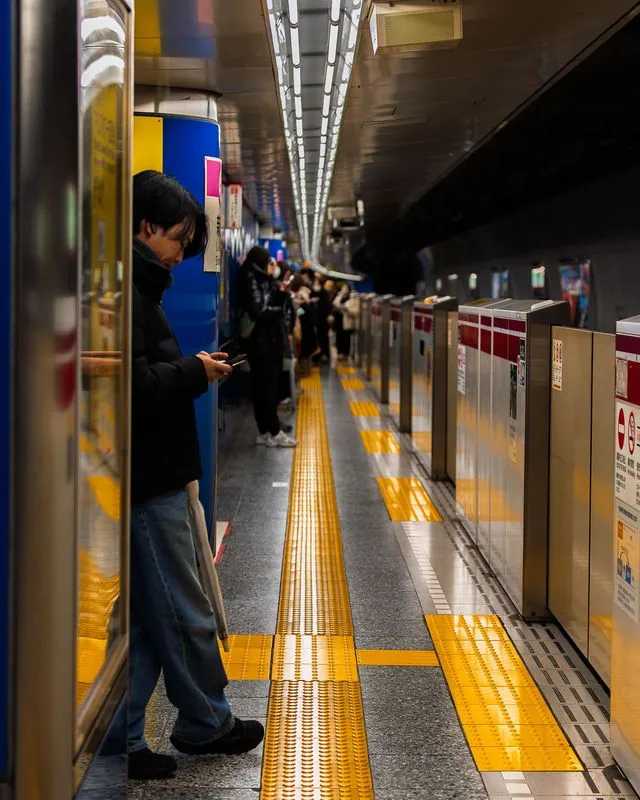 absorbed in his phone while the platform glows yellow around him