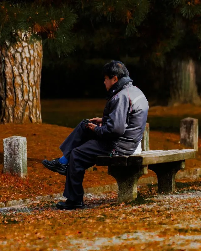 a man on a stone bench, absorbed in whatever is in his hands
